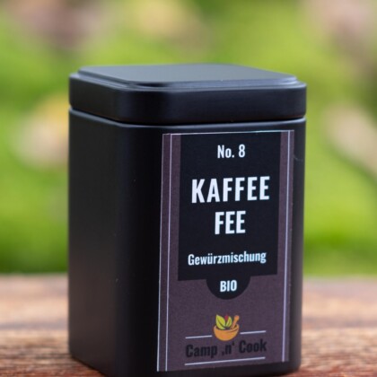 No. 8 KaffeeFee bio Gewürzmischung steht auf dem Etikett einer schwarzen quadratischen Dose. Die Grundfarbe des Etiketts ist Aubergine, der Schriftzug weiß auf schwarzem Hintergrund. Die Dose steht auf einem rustikalen Holzbrett mit grünem natürlichen Hintergrund.