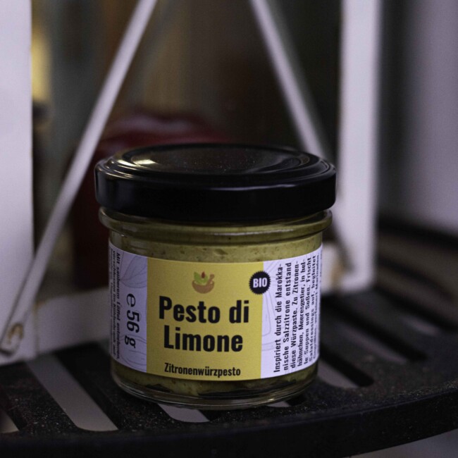 Pesto di Limone Zitronenpesto bio steht auf einem gelben Etikett. Das Glas ist mit einem schwarzen Deckel versehen und das goldgelbe Pesto scheint oben und unten durch das Glas.