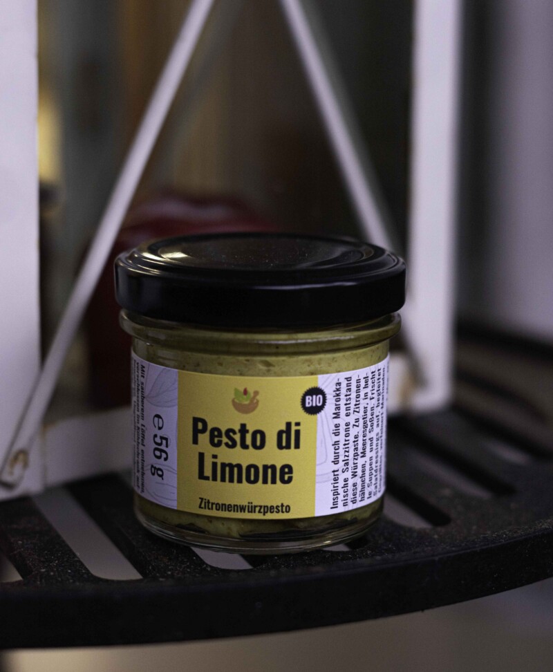 Pesto di Limone Zitronenpesto bio steht auf einem gelben Etikett. Das Glas ist mit einem schwarzen Deckel versehen und das goldgelbe Pesto scheint oben und unten durch das Glas.